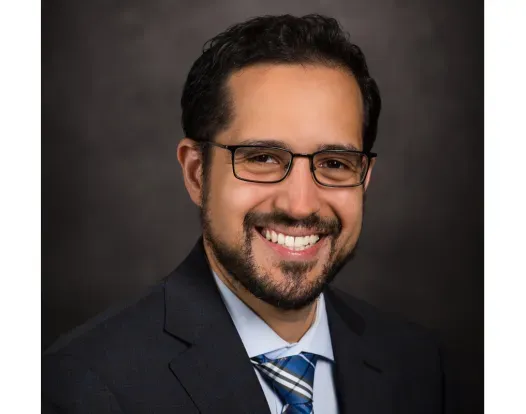Dr. Pavlos Msaouel headshot; he is smiling facing forward against a dark-gray background.