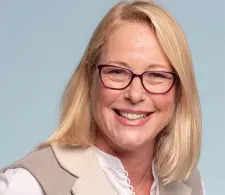 Dr. Amy Peterson headshot. She has shoulder-length blonde hair and is wearing glasses, smiling facin forward against a light-gray background and wearing a white/tan shirt.