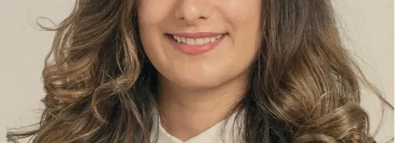 Dr. Bahar Laderian, wearing a black blouse with a white collar. She has arm-length wavy brown hair and is smiling facing forward.