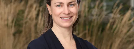 Dr. Michaela Higgins headshot. She smiling facing forward with arms crossed and is outdoors.