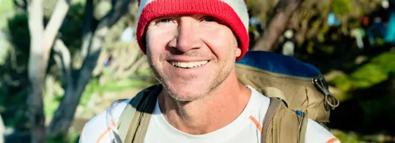 Sean Swarner in an outdoor setting wearing a climber backpack, smiling facing forward