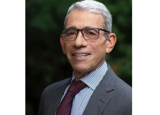 Dr. Eric P. Winer headshot. He is smiling facing forward. He has white hair, is wearing glasses, and is in a gray suit.