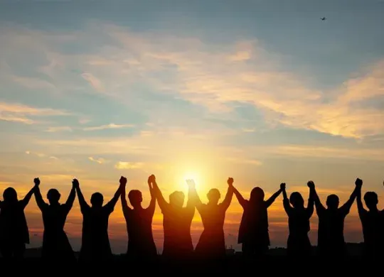 Silhouettes of people holding hands up and looking into the sunset