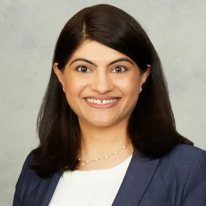 Dr. Surbhi Sidana headshot. She is smiling facing forward. She is wearing a dark blue blazer with a white blouse, as well as a necklace. She has shoulder-length dark brown hair.