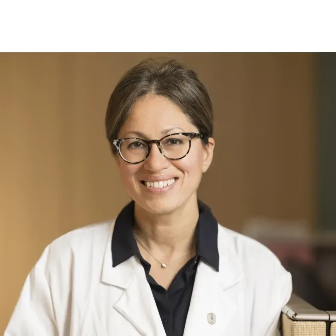 Headshot of Dr. Shanu Modi in a clinical sitting wearing a white coat, glasses, and brown hair. She is smiling facing forward.