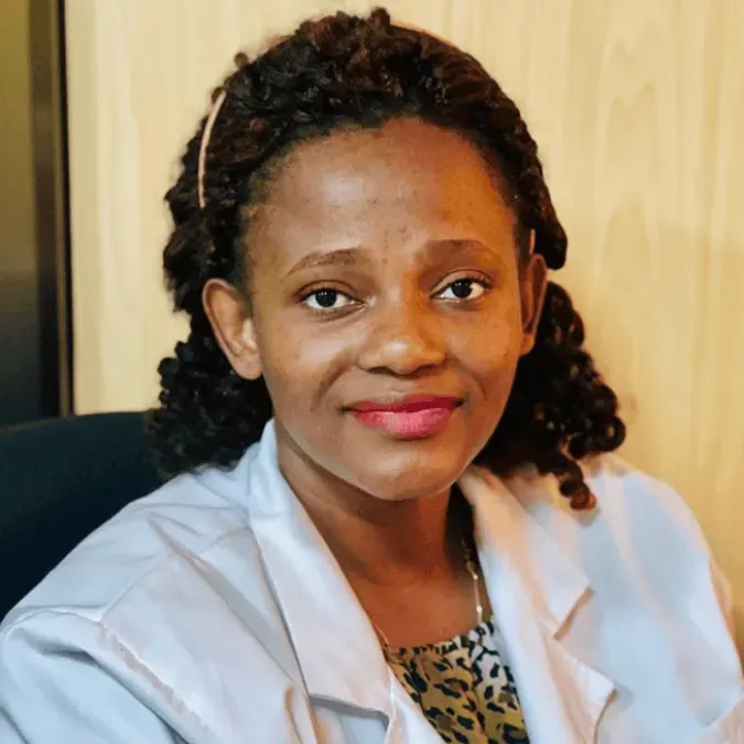 Dr. Sarah Nyagabona in a white coat and smiling facing forward in a clinical setting.